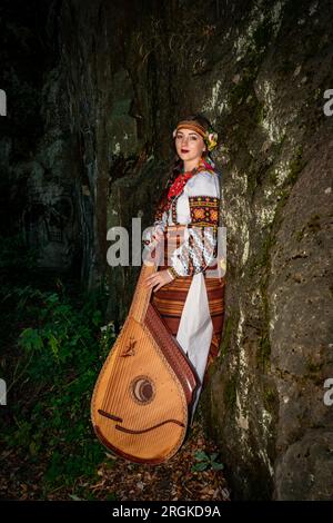 Un musicista ucraino in abiti nazionali sta con una bandura appoggiata su una roccia Foto Stock