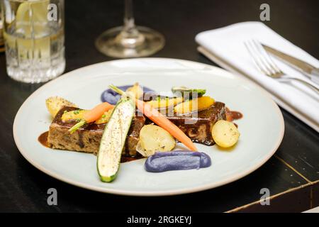 Angolo di piatto alto con delizioso foie gras servito con verdure assortite e guarnito con salsa sul tavolo nel ristorante Foto Stock