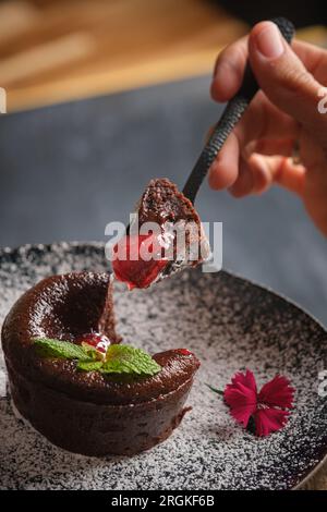 Angolo alto di persona anonima che prende un pezzo di cioccolato fondente con marmellata di frutti di bosco dal piatto con zucchero a velo Foto Stock