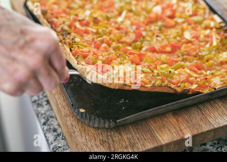 Dall'alto del raccolto cucinano tagliere di legno affettando appetitose pizze vegetariane al forno in cucina Foto Stock