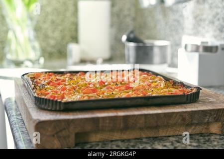 Deliziosa pizza fatta in casa con salsa di pomodoro ed erbe aromatiche poste su un tagliere di legno in cucina Foto Stock