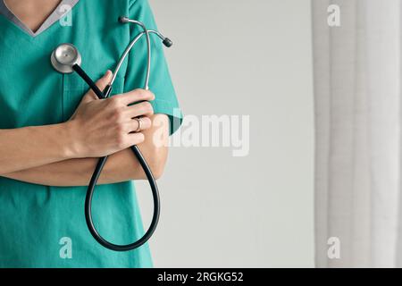 Crop medico femminile irriconoscibile in uniforme medica con braccia ripiegate e stetoscopio su sfondo chiaro Foto Stock