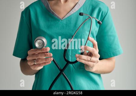 Crop medico femminile irriconoscibile in uniforme medica verde che dimostra stetoscopio con campana e tubi in luce diurna Foto Stock