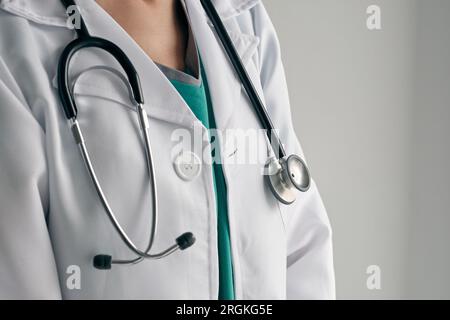 Crop anonimo medico femminile in uniforme medica bianca con stetoscopio professionale su sfondo chiaro di giorno Foto Stock