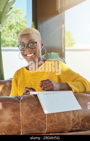 Ritratto di una donna afroamericana sorridente che scrive nel diario seduto sul divano a casa Foto Stock