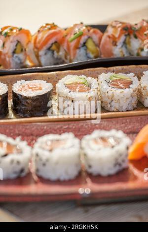 Dall'alto, primo piano dell'appetitoso sushi con panini Philadelphia e California e tekkamaki serviti su vassoi di ceramica posti in fila Foto Stock