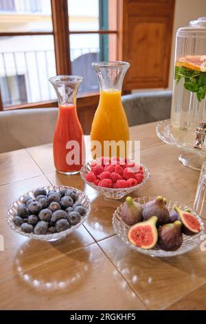 Buffet di fichi dolci lamponi mirtilli e bevande dolci e sane servite in vetreria su un tavolo di legno nella luminosa sala riunioni Foto Stock