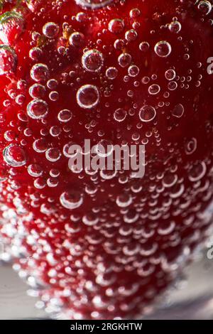 Chiudi la fragola intera ricoperta di bolle di biossido di carbonio sul fondo del bicchiere con una bevanda analcolica Foto Stock