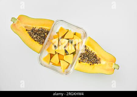 Vista dall'alto della pila di cubetti di papaya maturi collocati in un contenitore di vetro tra la frutta tagliata a metà su sfondo bianco Foto Stock