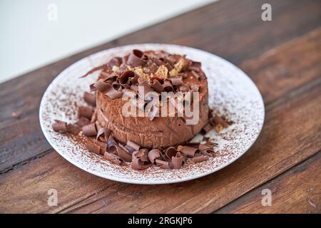 Angolo alto di deliziosa torta al cioccolato guarnita con scaglie di cioccolato e spruzzi serviti su un piatto bianco su un tavolo di legno Foto Stock