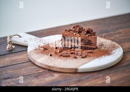 Gustosa torta al cioccolato decorata con cacao in polvere e scaglie servite su un tagliere posto su un tavolo di legno Foto Stock