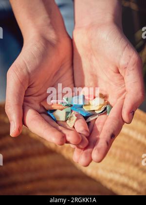 Vista dall'alto delle mani di un maschio anonimo che mostra pezzi di plastica colorati mentre raccoglie i rifiuti di plastica da riciclare all'aperto nelle giornate di sole Foto Stock