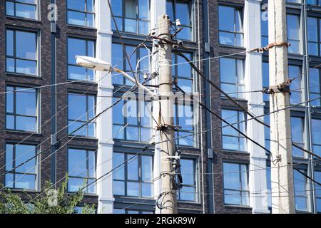 Palo cittadino con vari cavi e fili e illuminazione stradale sullo sfondo della facciata di un edificio residenziale in Ucraina in estate Foto Stock