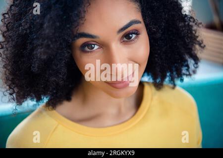 Foto ravvicinata di una donna piacevole soddisfatta del buon umore con un'ampia vestibilità gialla a maniche lunghe che ti sorride in casa Foto Stock