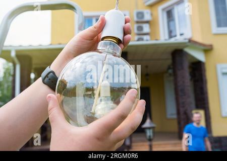 lampada a ncandescenza e mani dei bambini da vicino nel cortile in una giornata di sole Foto Stock