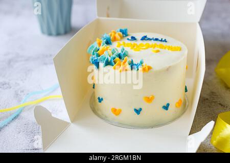 Torta bento alla moda con un'iscrizione blu-gialla in ucraino "buon compleanno" su sfondo chiaro. Torta di compleanno, torta Bento per due Ukrai Foto Stock