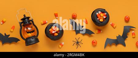 Composizione con gustosi grani di caramelle, lanterna e decorazioni di Halloween su sfondo arancione, vista dall'alto Foto Stock