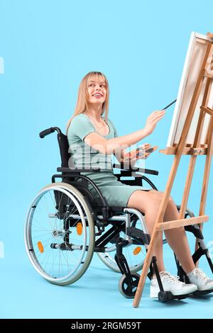 Giovane donna in sedia a rotelle dipinto su cavalletto su sfondo blu Foto Stock