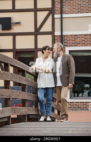 uomo e donna barbuti felici che si guardano, coppia anziana, in piedi vicino al ponte, romanticismo Foto Stock