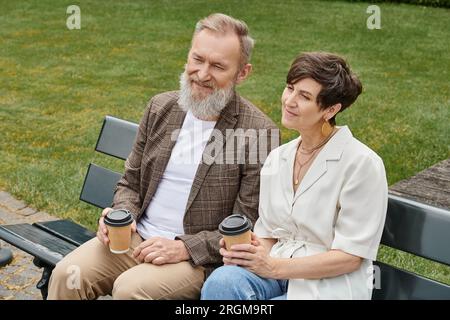 un uomo e una donna anziani felici seduti sulla panchina, con tazze di carta e caffè, una coppia anziana, romanticismo Foto Stock