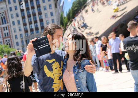 Una coppia usa il cellulare per scattare una foto davanti alla scultura "The Bean" a Grant Park, Chicago, Illinois, il 6 luglio 2018. Un rapporto dei media "Common Sense" ha rilevato che il 75% degli americani dice di essere dipendente dai loro smartphone controllandoli all'incirca una volta ogni 10 minuti. Gli esperti suggeriscono che la dipendenza da smartphone può avere un impatto negativo sul cervello e portare a depressione, ansia, disturbi comportamentali e compulsivi. (Foto di: Alexandra Buxbaum/Sipa USA) credito: SIPA USA/Alamy Live News Foto Stock