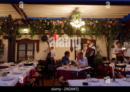 I musicisti suonano al famoso ristorante Three Hats di fronte agli ospiti in via Skadarlija in una serata estiva a Belgrado, Serbia. 10 agosto 2023.. Foto Stock