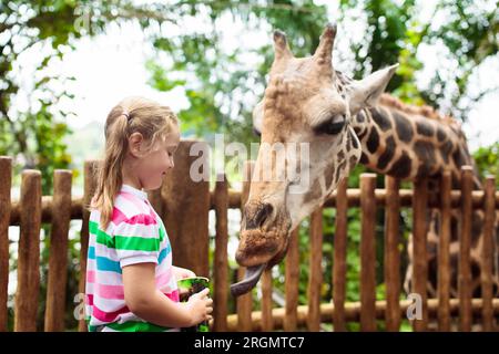 Giraffa per l'alimentazione della famiglia nello zoo. I bambini nutrono le giraffe nel parco safari tropicale durante le vacanze estive a Singapore. I bambini guardano gli animali. Foto Stock