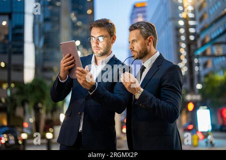 Affari notturni in città. Gli uomini d'affari controllano le loro e-mail e esaminano documenti importanti su tablet durante la notte in città. Affari, tecnologia e persone Foto Stock