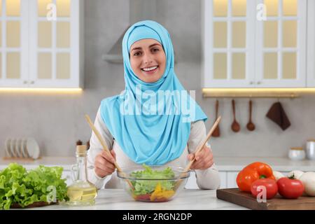 Donna musulmana che prepara una deliziosa insalata con verdure al tavolo bianco in cucina Foto Stock