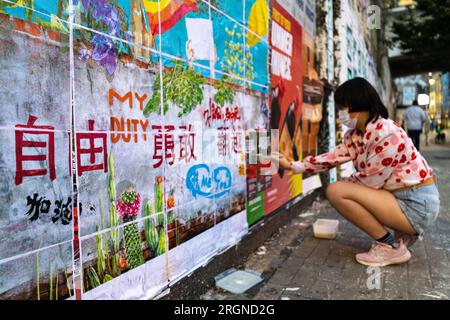 Un attivista anti-Pechino, Apple, della China Deviants, attacca un contro-murale a Brick Lane. "Brick Lane a East London, storicamente celebrata per la sua eclettica Street art, è stata recentemente coinvolta in una controversa guerra dei graffiti. Il conflitto è iniziato sabato 5, quando un gruppo di artisti ha mostrato i "12 valori socialisti fondamentali" del Partito Comunista Cinese. In 24 caratteri cinesi rossi in grassetto su una parete di 100 metri. Questi valori sono "prosperità”, "democrazia”, "civiltà” e "armonia”; i valori sociali di "libertà”, "uguaglianza”, "giustizia” e "Stato di diritto”; e i valori individuali di "patrio” Foto Stock