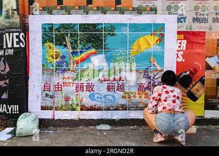 Un attivista anti-Pechino, Apple, della China Deviants, attacca un contro-murale a Brick Lane. "Brick Lane a East London, storicamente celebrata per la sua eclettica Street art, è stata recentemente coinvolta in una controversa guerra dei graffiti. Il conflitto è iniziato sabato 5, quando un gruppo di artisti ha mostrato i "12 valori socialisti fondamentali" del Partito Comunista Cinese. In 24 caratteri cinesi rossi in grassetto su una parete di 100 metri. Questi valori sono "prosperità”, "democrazia”, "civiltà” e "armonia”; i valori sociali di "libertà”, "uguaglianza”, "giustizia” e "Stato di diritto”; e i valori individuali di "patrio” Foto Stock