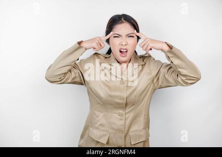 Una lavoratrice civile pazza che indossa un'uniforme marrone è così stressata. Concetto di lavoro eccessivo da parte dei dipendenti governativi indonesiani. Foto Stock