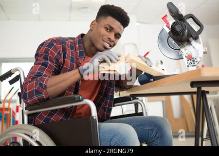 uomo in sedia a rotelle che sfrega il legno con carta vetrata Foto Stock