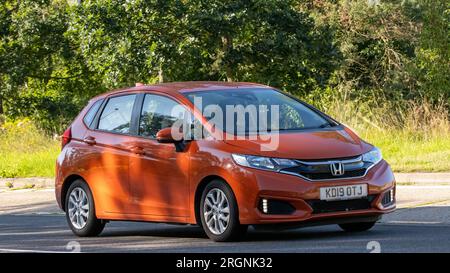 Milton Keynes, Regno Unito - 10 agosto 2023: 2019 auto Honda Jazz arancione che guida su una strada di campagna inglese. Foto Stock