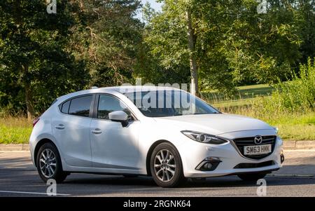 Milton Keynes, Regno Unito - 10 agosto 2023: 2014 auto Mazda 3 bianca che guida su una strada di campagna inglese. Foto Stock