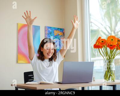Una giovane donna latina che si sente entusiasta di alzare i pugni celebra la promozione o la ricompensa della carriera, gli studenti seduti alla scrivania ricevono notizie online, grandi risultati lavoro di successo o concetto di studio Foto Stock
