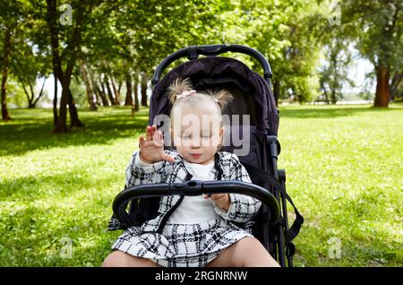 Bambino in passeggino su una passeggiata nel parco estivo. Adorabile bambina seduta in poltrona. Bambino in buggy Foto Stock