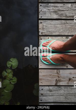 Sopra i piedi di una donna con sandali sul molo di legno indossato sul lago. Foto Stock