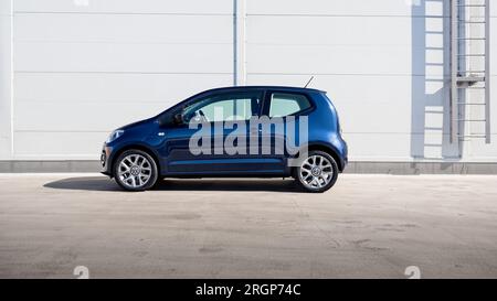 Berlina compatta blu Volkswagen UP! vista del profilo laterale parcheggiata vicino alla parete grigia Foto Stock