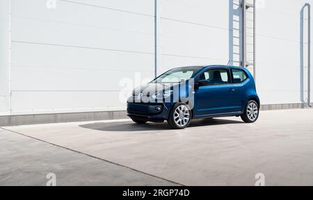 Berlina compatta blu Volkswagen UP! vicino alla parete grigio chiaro, vista a tre quarti Foto Stock