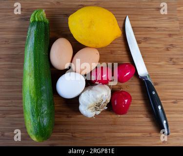 Prodotti freschi e uova su tagliere di legno con coltello Foto Stock