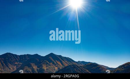 Il sole splende e i raggi nel mezzo del cielo blu pomeridiano sulle cime delle montagne Foto Stock