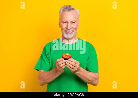 Foto dell'allegro e funky ragazzo vestito di maglietta verde che mangia un piccolo cupcake isolato di colore giallo Foto Stock