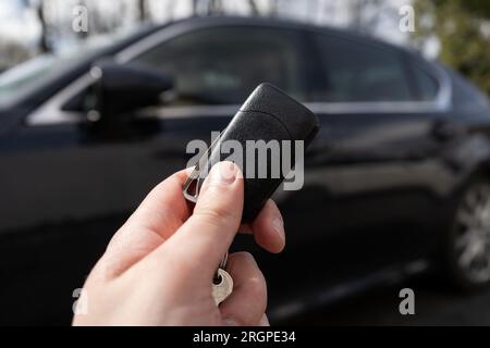 Mano dell'uomo che tiene la chiave dell'auto remota, accanto a un veicolo nero. Foto Stock