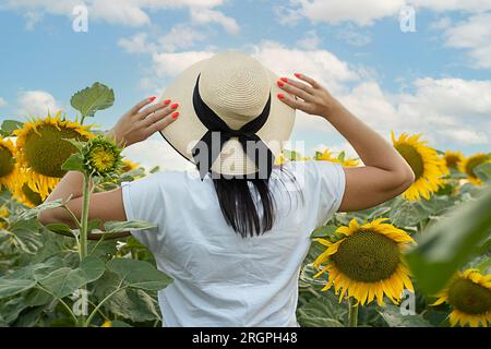 Un simbolo di pace. Concetto di Ucraina. Una ragazza con un cappello di paglia si trova in un campo con girasoli gialli, contro un cielo blu. Vista dal retro. Niente faccia. Foto Stock