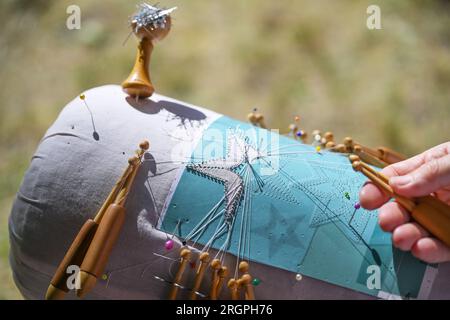 Processo di pizzo a forma di stella, le mani gestiscono i fili con l'aiuto di bobine di legno per attorcigliarli intorno ai perni sulla pillola di pizzo Foto Stock