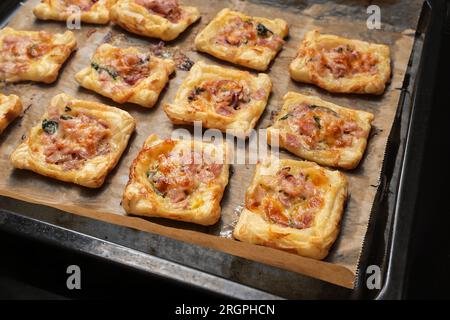 Quadrati di pasta sfoglia al forno con prosciutto, spinaci e formaggio su un vassoio con carta da forno, stuzzichini per un buffet caldo o freddo, spazio fotocopie, sel Foto Stock