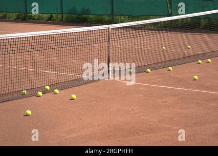 Campo da tennis vuoto in terra battuta e molte palline gialle prima della rete Foto Stock