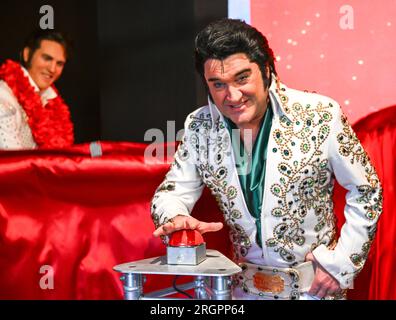 Berlino, Germania. 11 agosto 2023. L'artista di Elvis Grahame Patrick (r) della serie "Stars in Concert" si trova nel museo delle cere Madame Tussauds di Berlino e preme il pulsante rosso per svelare una figura di Elvis appena restaurata. Fino ad ora, la figura era raffigurata nell'uniforme dell'esercito degli Stati Uniti, mentre il cantante la indossava nel 1958 durante il suo servizio militare nella Germania Ovest. Dopo 15 anni al servizio del museo delle cere, Elvis ha ricevuto negli ultimi mesi un nuovo vestito e un nuovo taglio di capelli. Credito: Soeren Stache/dpa/Alamy Live News Foto Stock