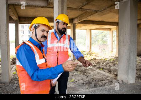 Due ingegneri civili o architetti indiani che indossano un casco e un giubbotto che lavorano in cantiere, nel settore immobiliare. Foto Stock